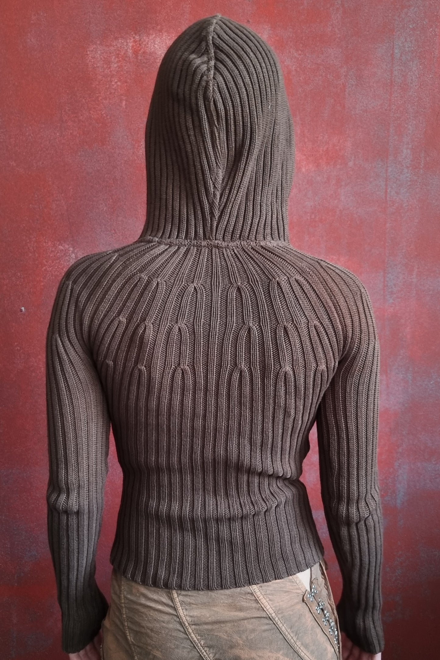model wearing a ribbed knit hoodie with 2 way zipper against a textured red background